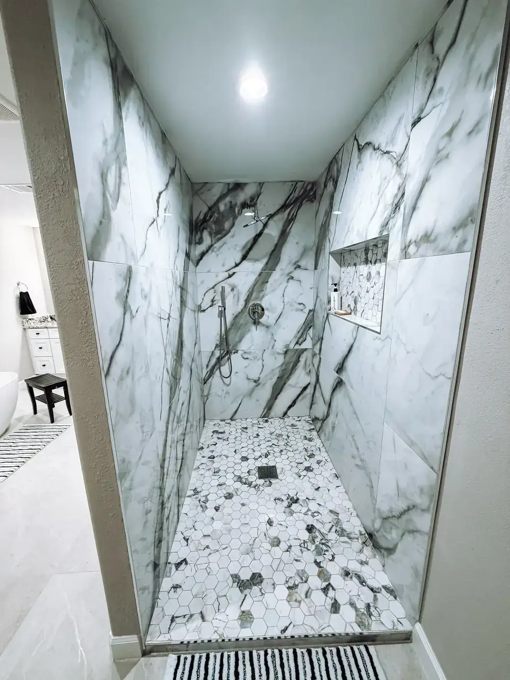 Walk-in shower lined floor to ceiling in dramatic white and grey marble-look slab, with a matching bench and a linear drain