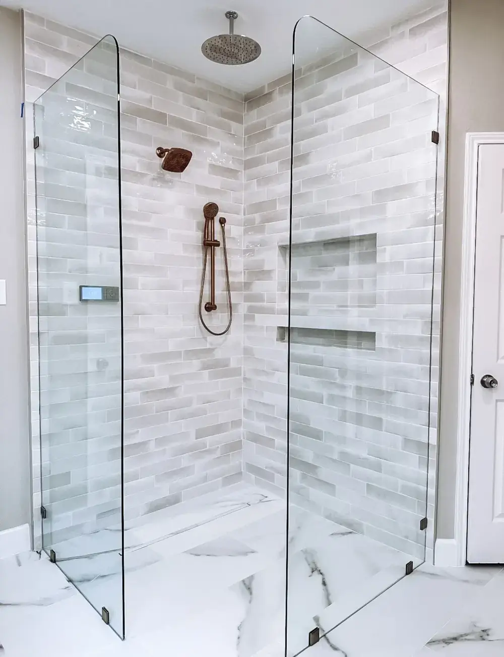 Frameless glass corner shower with a rainfall showerhead, handheld sprayer, stacked stone-look wall tile, and a freestanding tub alongside