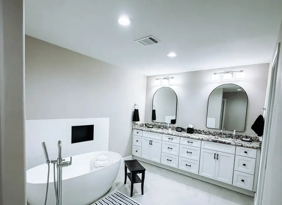 Remodeled master bathroom with a freestanding soaking tub, a white shaker double vanity, and arched black-framed mirrors