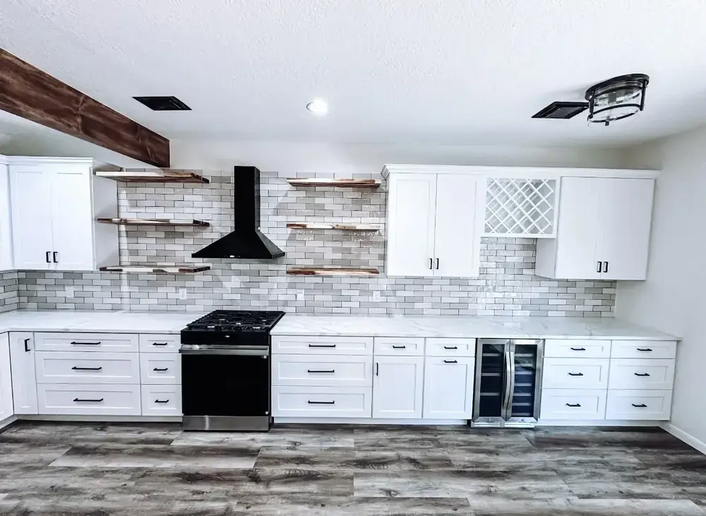 Remodeled kitchen with white shaker cabinets, black chevron range hood, floating wood shelves, built-in lattice wine rack, and marble-look quartz countertops