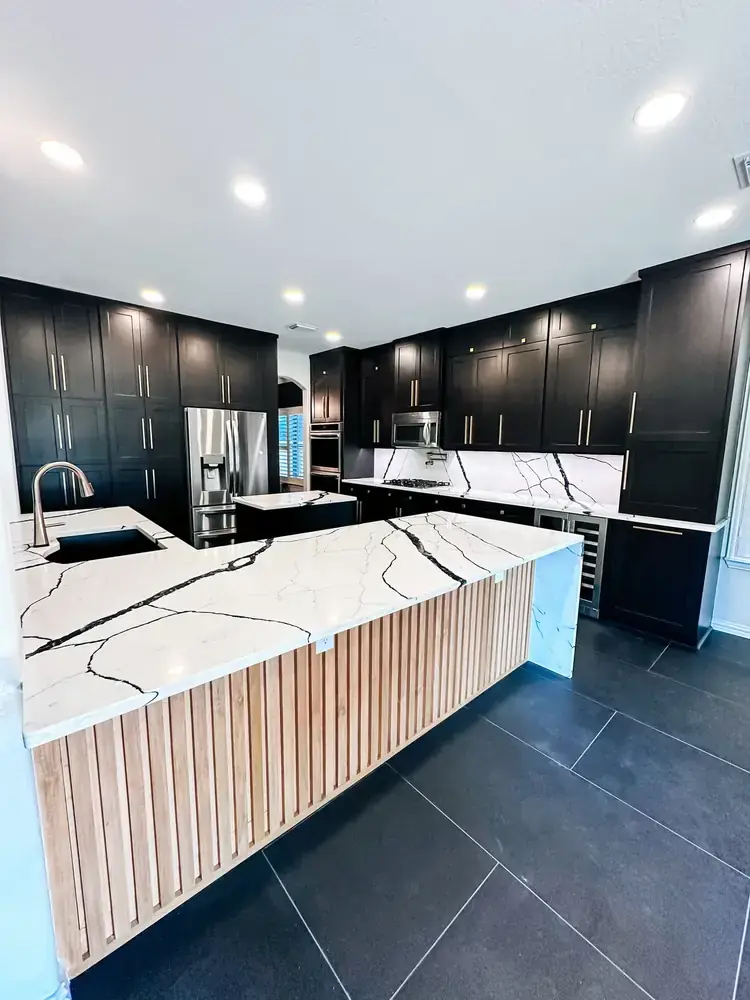 High-end kitchen with black shaker cabinets, brass hardware, fluted white-oak island, and black-veined waterfall quartz