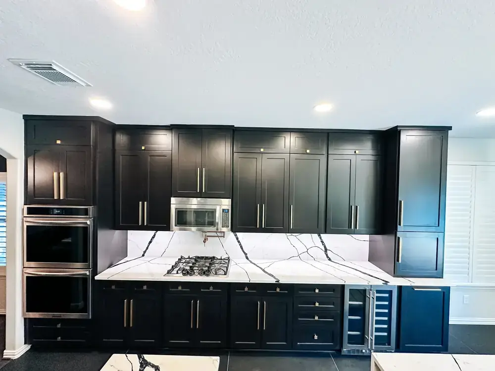 Kitchen remodel with floor-to-ceiling black cabinetry, brass hardware, double wall ovens, and bold veined quartz backsplash