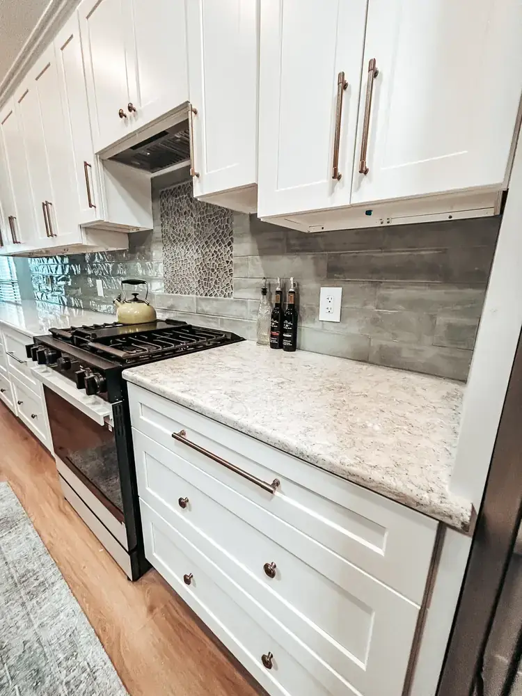 Refreshed kitchen with white shaker cabinets, brass pulls, cream quartz countertops, and gray subway-tile backsplash