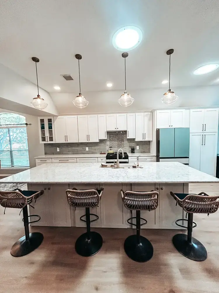 Large white kitchen island with quartz countertop, four rattan barstools, and schoolhouse pendant lights